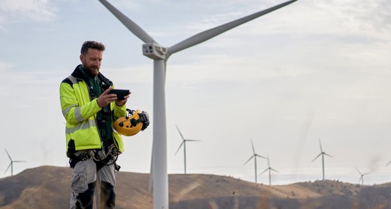 An engineer looking at a tablet standing near to wind turbines