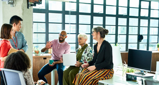 Six people in relaxed conversation with a laptop and coffee