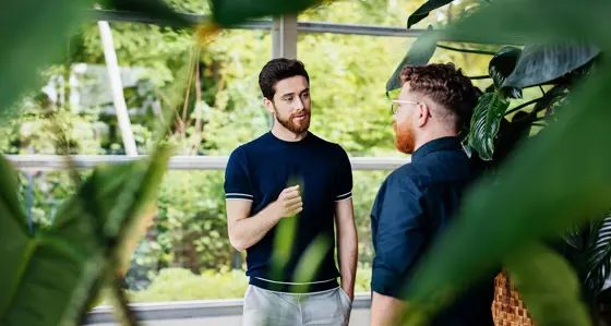 Two men chatting in a greenhouse surrounded by plants
