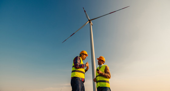 Two engineers in discussion in front of a wind turbine