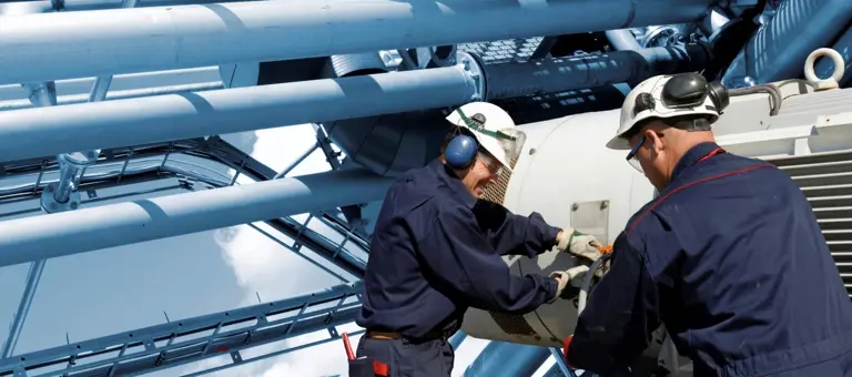 Two engineers in hard hats and ear defenders inspecting equipment