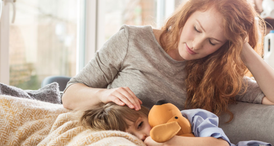 A boy holding a cuddly toy resting on his mother's lap