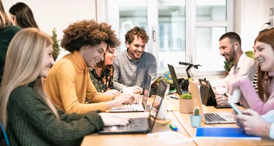 A group of laughing and smiling interns sitting around a table with their laptops