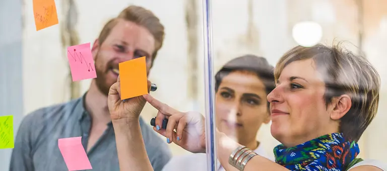 Colleagues writing on post-its on a transparent wall