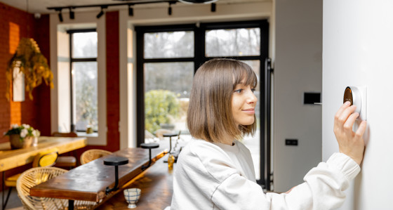 A woman at home adjusting a digital thermostat