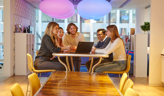 A group of colleagues sitting around a laptop in a relaxed office setting