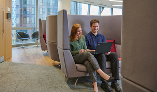 Two colleagues looking at laptop while sitting on a sofa in a relaxed and comfortable office environment