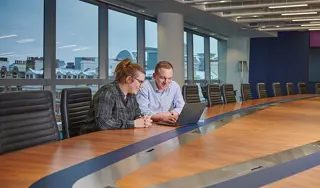 Two colleagues looking at a laptop in a board room