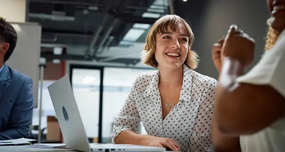 Three happy multiracial business people wearing businesswear smiling during discussion at meeting in office