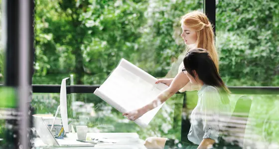 A pair of women discussing a hand-held plan with lush green vegetation in the background