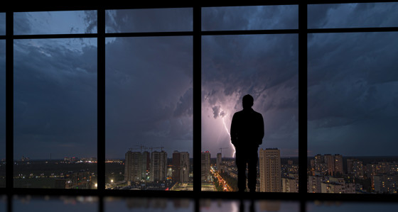 Man in office building looking out at lightning storm