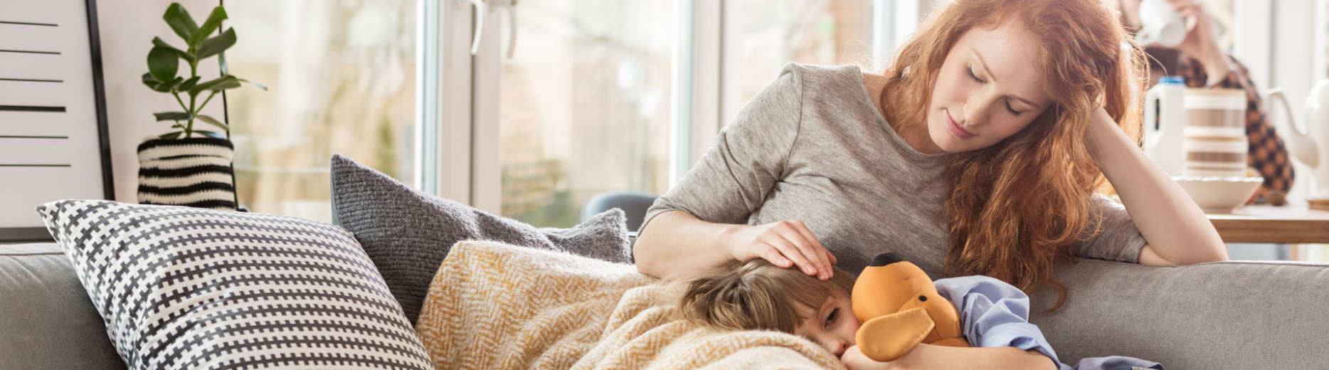 A boy holding a cuddly toy resting on his mother's lap