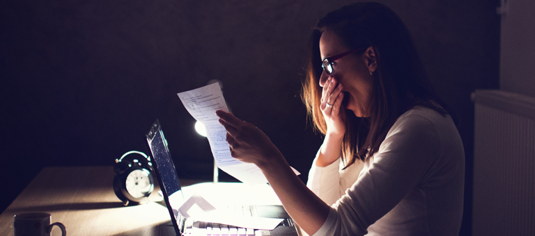 A woman yawning while reading a report in front of a laptop