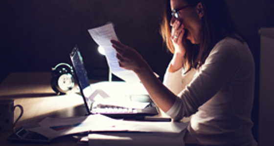 A woman yawning while reading a report in front of a laptop