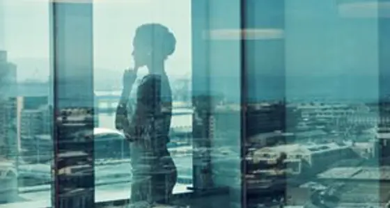 A thoughtful woman looking out of an office window over the city skyline