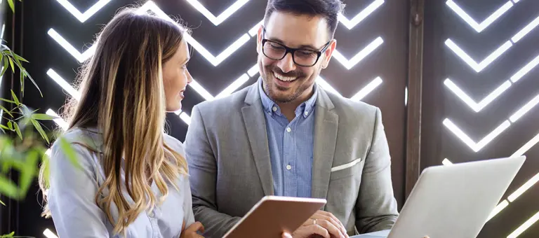 Two smiling people looking at a tablet with plants next to them