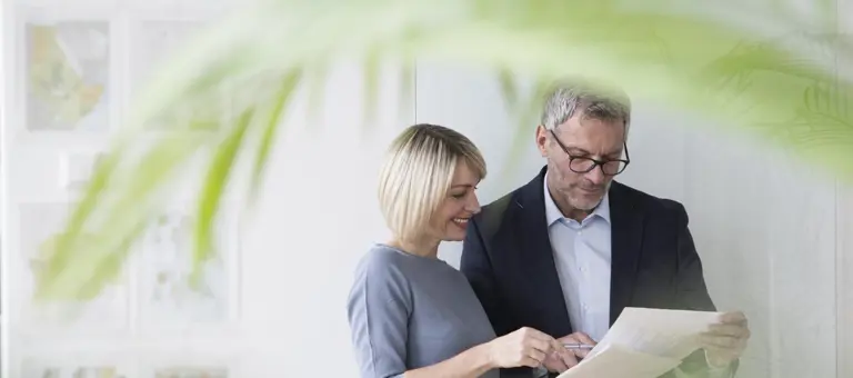 Two people looking at some paper with a palm frond in the foreground