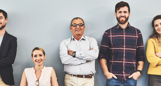 Seven smiling people in front of a grey wall