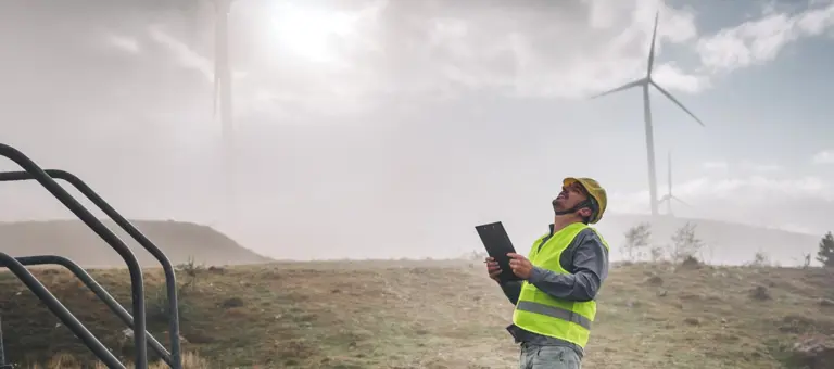 A man with a clipboard looking upwards at a wind turbine