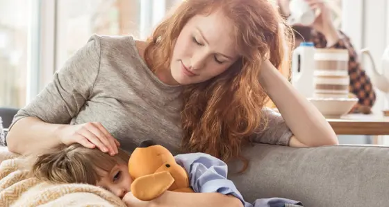 A boy holding a cuddly toy resting on his mother's lap