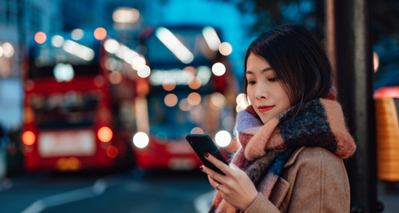 Women next to London bus stop looking at phone at night