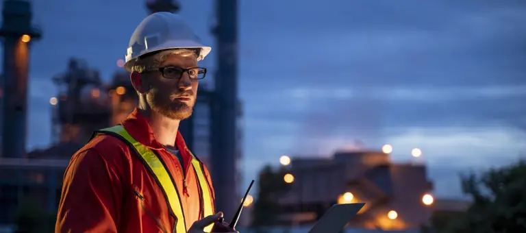 A man dressed ijn high-vis and hard hat standing in front of a refinery