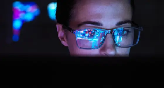 Woman in a dark room with screen monitor reflecting in her glasses
