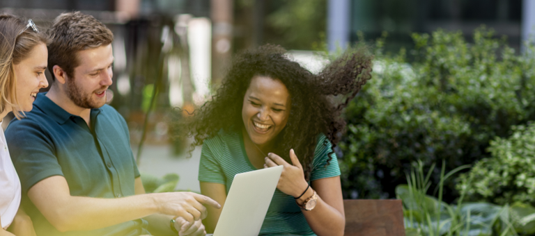 Three people sitting outside looking at a laptop