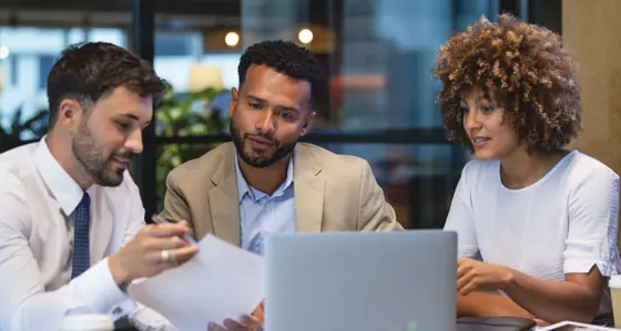 Three colleagues discussing plans in front of a laptop