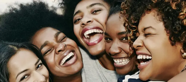 A group of black girlfriends hug and laugh