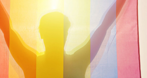  A silhouetted person holding up a rainbow flag in front of them