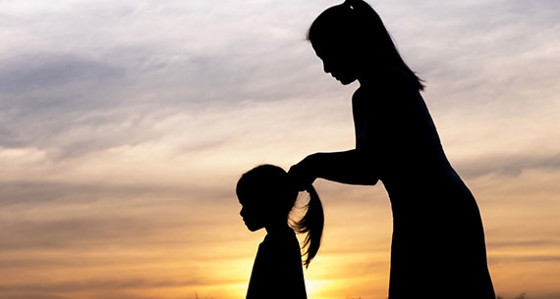 A mum putting her daughter's hair in a pony-tail silhouetted by the setting sun