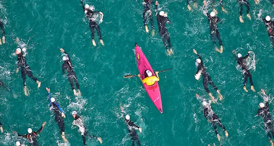 A pink kayak paddling among wet-suited sea swimmers