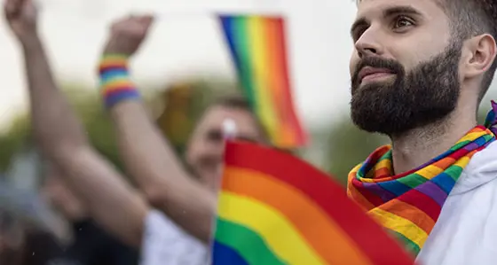 A man in a crowd wearing a rainbow-coloured scarf