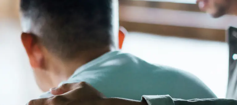 A man standing with his arm around someone comforting them