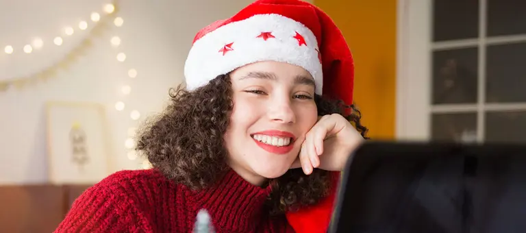 A woman in a Santa ha at her desk with Christmas decorations in the background