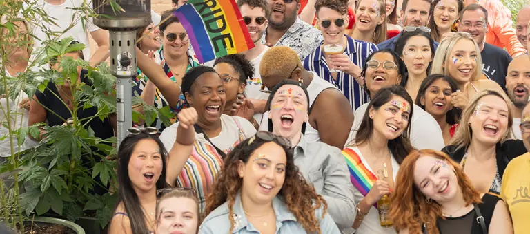 A group of smiling people with Pride rainbow flags